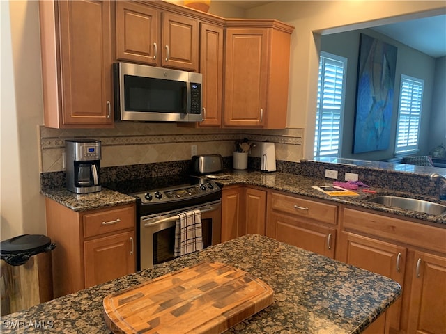 kitchen featuring stainless steel appliances, dark stone countertops, sink, and backsplash