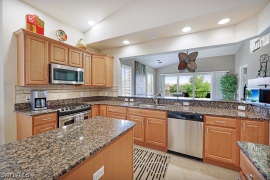 kitchen featuring dark stone counters, stainless steel appliances, sink, and lofted ceiling