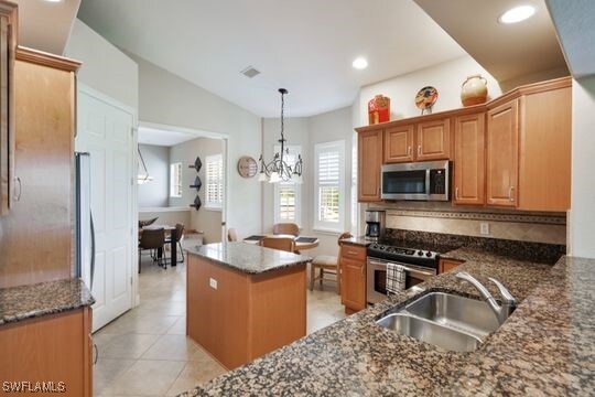 kitchen with appliances with stainless steel finishes, a kitchen island, pendant lighting, sink, and a notable chandelier