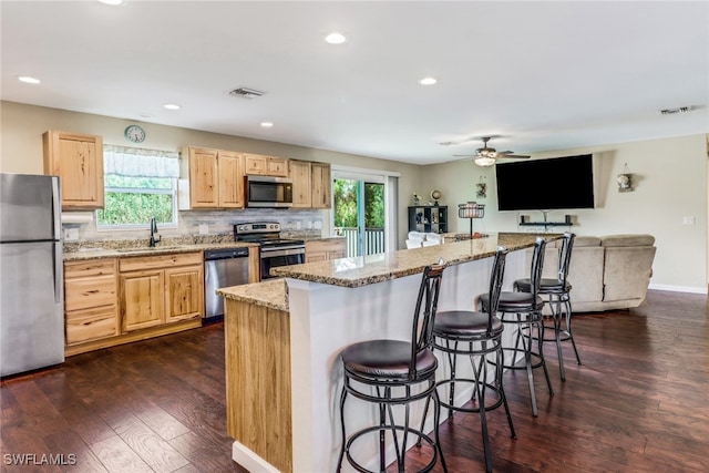 kitchen with stainless steel appliances, a wealth of natural light, a kitchen island, and dark wood-type flooring