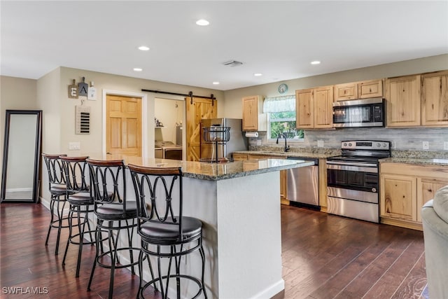 kitchen with appliances with stainless steel finishes, a barn door, a center island, and dark hardwood / wood-style flooring