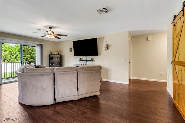 living room with ceiling fan, a barn door, and dark hardwood / wood-style flooring