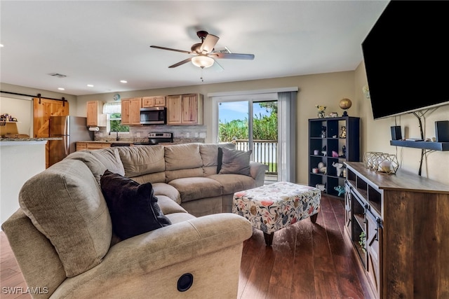 living room with ceiling fan, a barn door, and dark hardwood / wood-style flooring