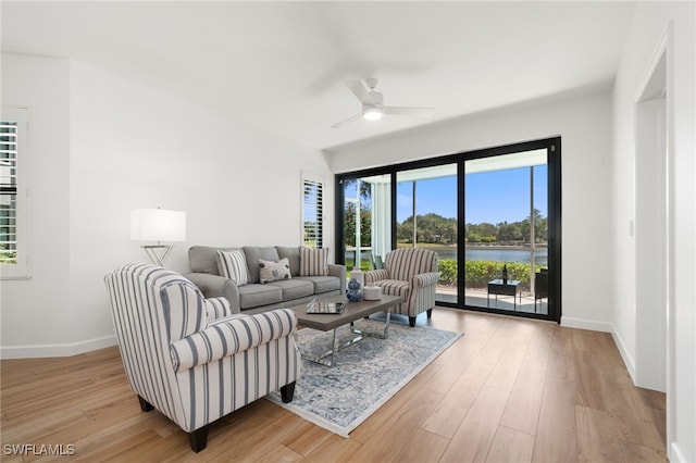living room with a ceiling fan, baseboards, light wood-style floors, and a water view