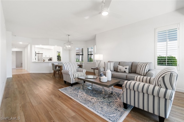 living room with a healthy amount of sunlight, light hardwood / wood-style floors, and ceiling fan with notable chandelier