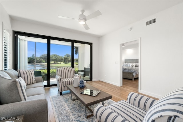 living area with light wood-style floors, baseboards, ceiling fan, and a water view