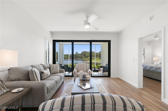living area with light wood-type flooring, a ceiling fan, baseboards, and a water view