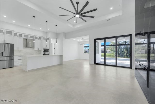 kitchen with white cabinets, appliances with stainless steel finishes, glass insert cabinets, open floor plan, and wall chimney range hood