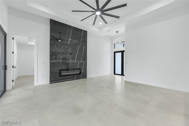 unfurnished room with recessed lighting, a raised ceiling, a high end fireplace, ceiling fan, and baseboards