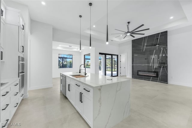 kitchen with white cabinets, a kitchen island with sink, a tray ceiling, a sink, and a high end fireplace