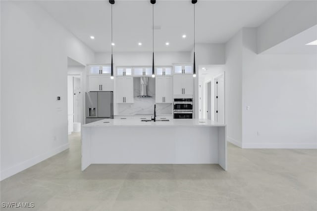 kitchen with hanging light fixtures, appliances with stainless steel finishes, wall chimney range hood, and white cabinetry