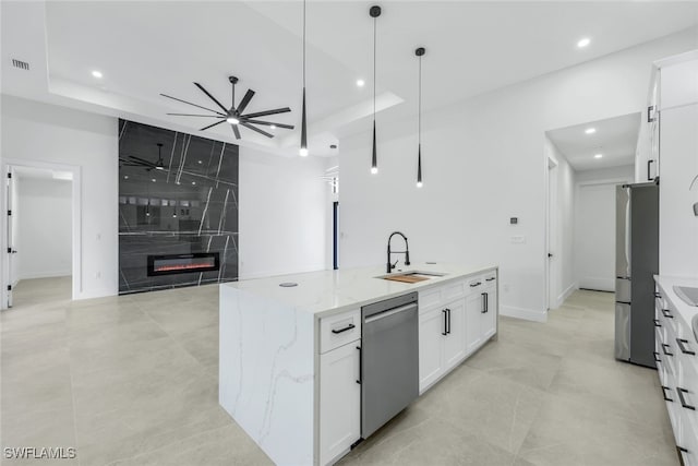 kitchen with light stone counters, stainless steel appliances, hanging light fixtures, white cabinetry, and a sink