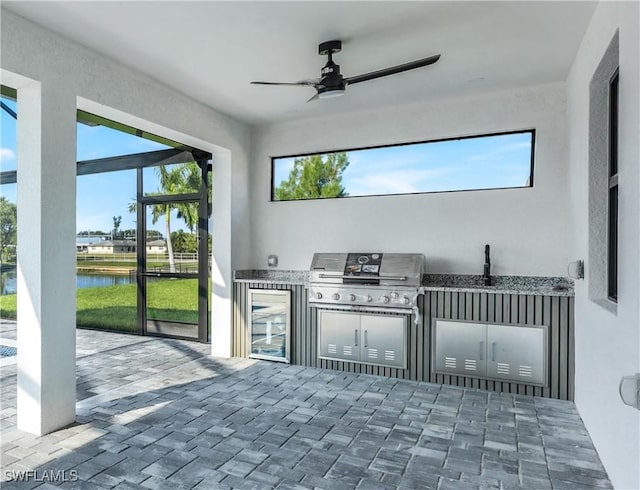 view of patio featuring exterior kitchen, a water view, a grill, and a ceiling fan