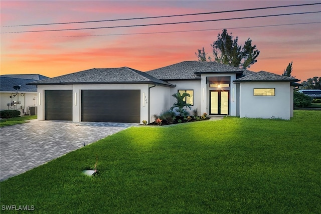 view of front facade featuring decorative driveway, stucco siding, central air condition unit, a lawn, and a garage