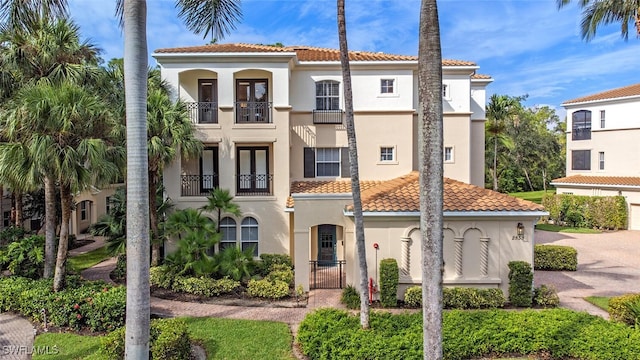 mediterranean / spanish home featuring a gate, a tile roof, a balcony, and stucco siding