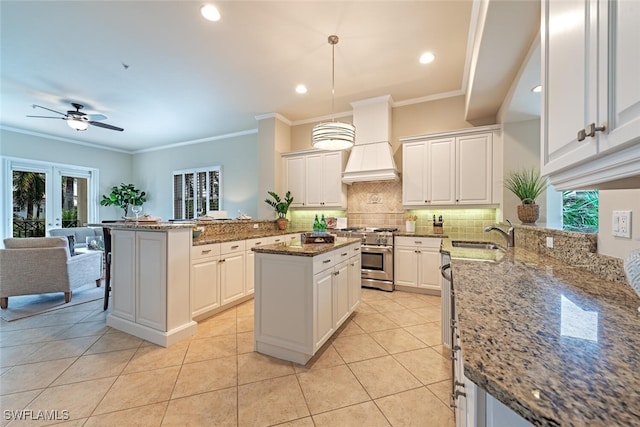 kitchen featuring decorative backsplash, high end range, premium range hood, a sink, and light tile patterned flooring