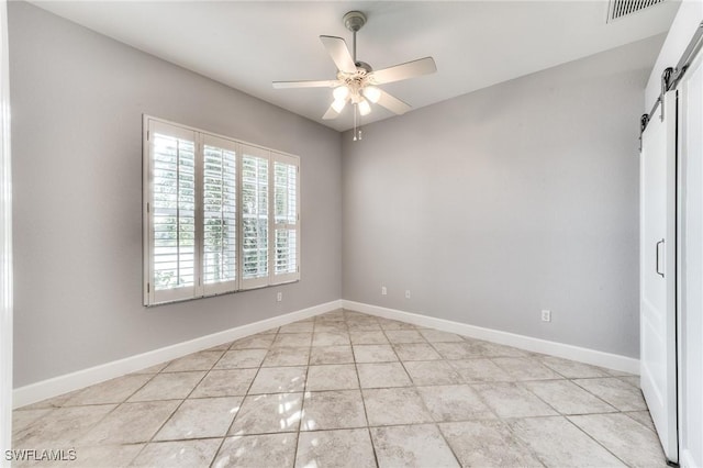 empty room featuring ceiling fan, a barn door, and light tile patterned floors