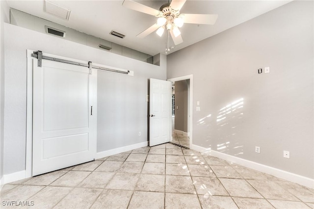 unfurnished bedroom featuring light tile patterned flooring, ceiling fan, and a barn door