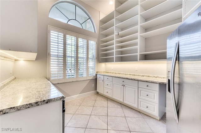 kitchen with light tile patterned floors, light stone countertops, white cabinets, and stainless steel refrigerator with ice dispenser