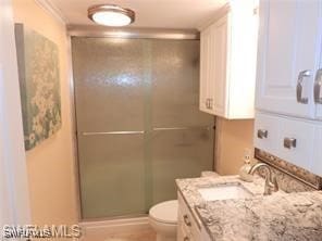 bathroom with ornamental molding, vanity, toilet, and a shower with door