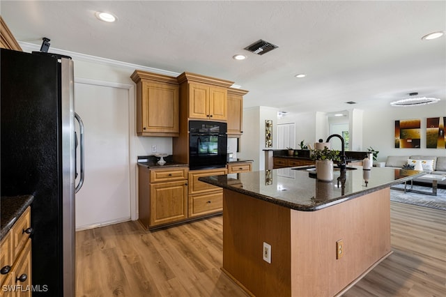 kitchen with ornamental molding, a center island with sink, oven, stainless steel refrigerator, and light hardwood / wood-style floors