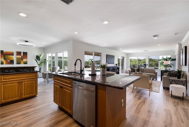 kitchen with an island with sink, dishwasher, light hardwood / wood-style flooring, dark stone counters, and sink