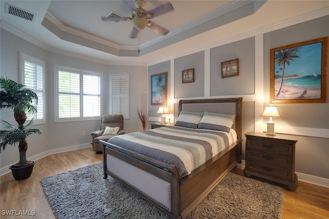 bedroom with light hardwood / wood-style flooring, ceiling fan, a raised ceiling, and crown molding