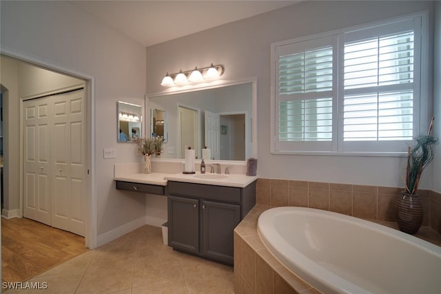 bathroom featuring tile patterned flooring, tiled bath, and vanity