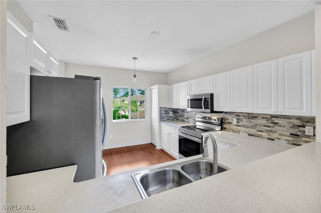 kitchen with pendant lighting, backsplash, white cabinetry, hardwood / wood-style flooring, and appliances with stainless steel finishes