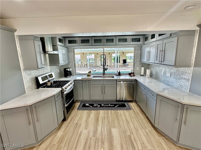 kitchen with sink, gray cabinetry, wall chimney range hood, stainless steel appliances, and light hardwood / wood-style floors