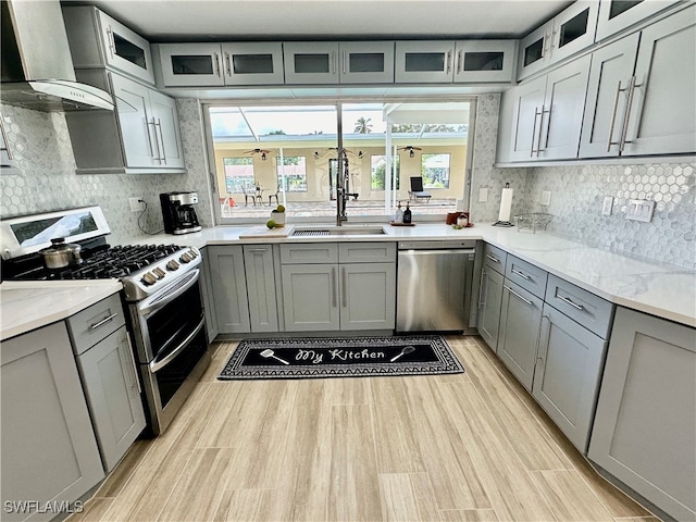 kitchen featuring appliances with stainless steel finishes, light stone counters, tasteful backsplash, sink, and wall chimney range hood