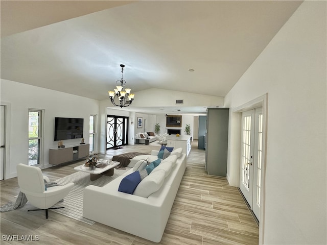 living room featuring lofted ceiling, an inviting chandelier, light hardwood / wood-style flooring, and french doors