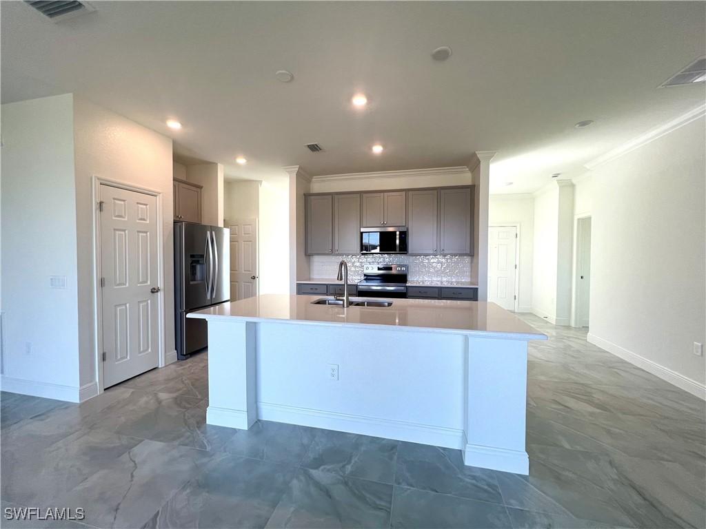 1303 NW 40th Pl, Cape Coral, FL 33993 - kitchen with stainless steel appliances, a sink, gray cabinetry, crown molding, and a center island with sink