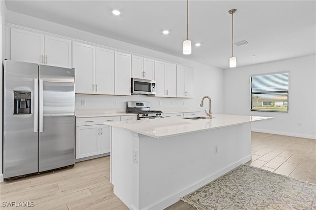 kitchen with sink, an island with sink, white cabinetry, appliances with stainless steel finishes, and decorative light fixtures