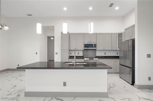 kitchen featuring pendant lighting, dark stone counters, sink, an island with sink, and appliances with stainless steel finishes