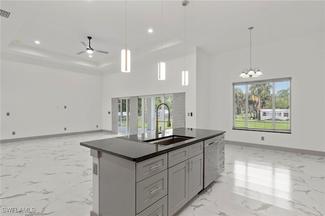 kitchen featuring an island with sink, sink, stainless steel dishwasher, a tray ceiling, and ceiling fan with notable chandelier