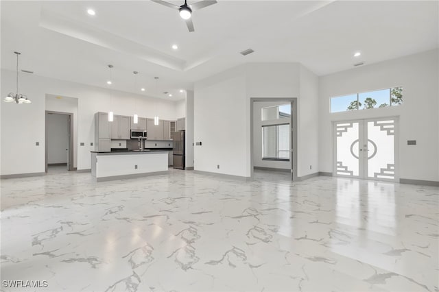 unfurnished living room featuring ceiling fan with notable chandelier, a high ceiling, and french doors