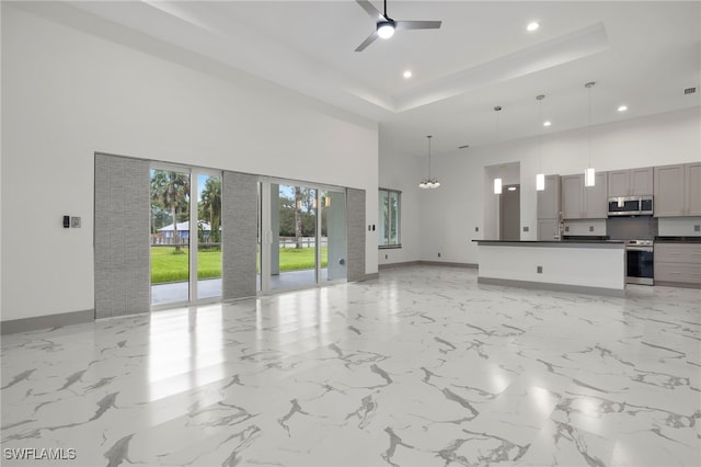 kitchen featuring ceiling fan, pendant lighting, gray cabinetry, stainless steel appliances, and a towering ceiling