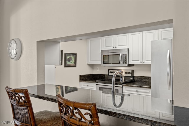 kitchen with white cabinets, appliances with stainless steel finishes, and dark stone counters