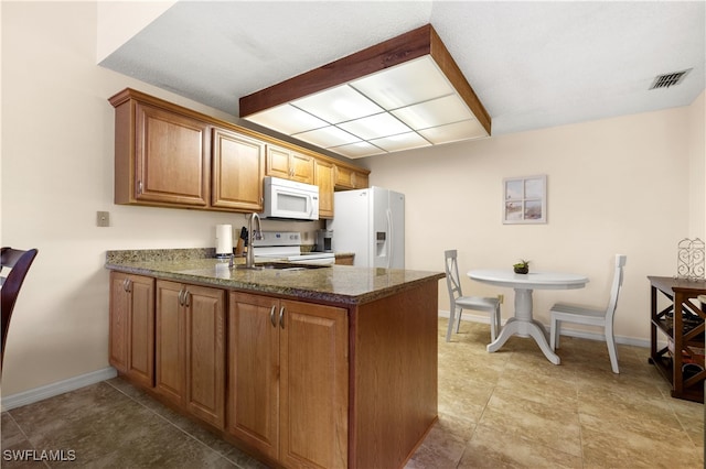 kitchen with dark stone counters, white appliances, and light tile patterned floors