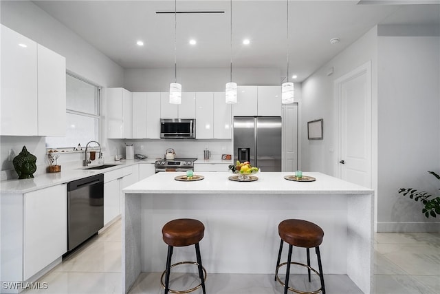 kitchen featuring white cabinetry, stainless steel appliances, a center island, decorative light fixtures, and sink