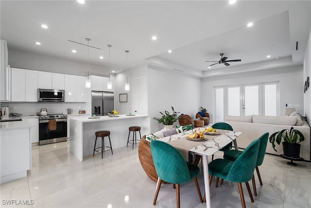 dining area with ceiling fan, a raised ceiling, and sink