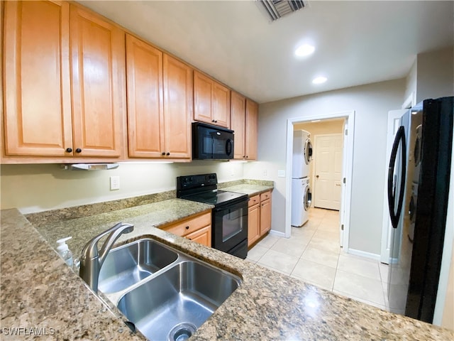 kitchen featuring light tile patterned floors, sink, stone countertops, black appliances, and stacked washer / drying machine