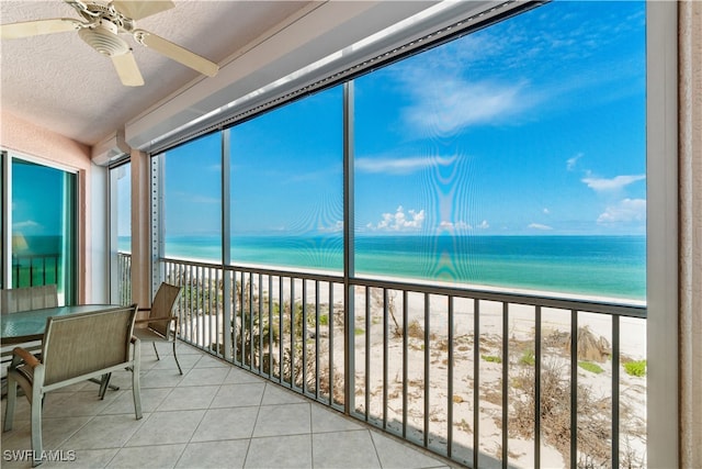 unfurnished sunroom featuring a water view, a beach view, ceiling fan, and a wealth of natural light