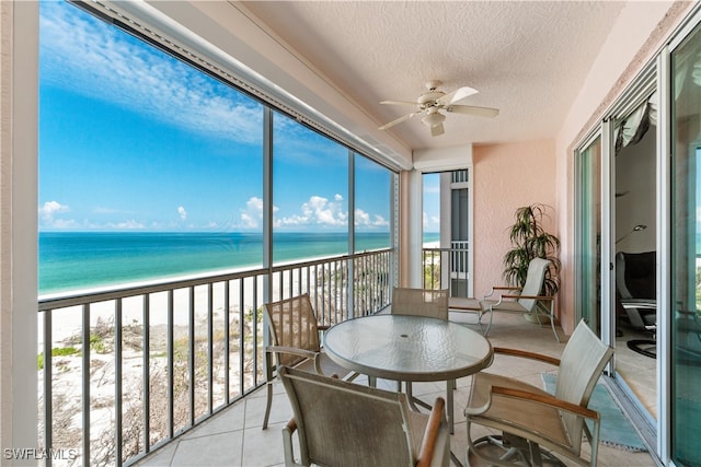 sunroom with a view of the beach, a water view, and ceiling fan