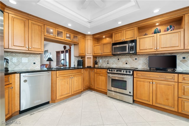 kitchen featuring sink, tasteful backsplash, stainless steel appliances, a tray ceiling, and dark stone counters