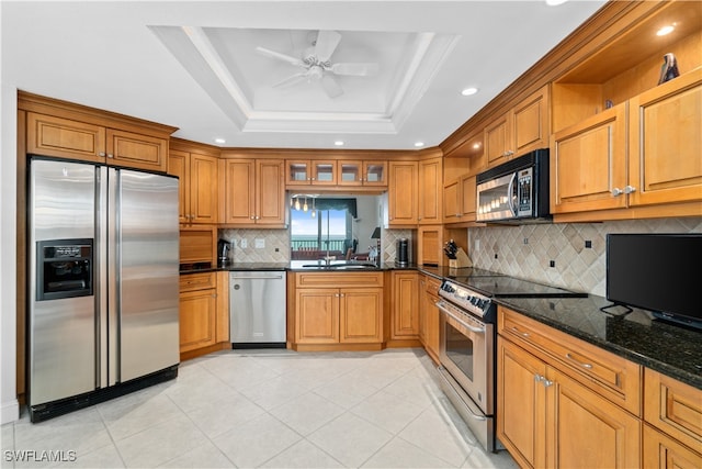 kitchen with sink, a raised ceiling, appliances with stainless steel finishes, dark stone countertops, and ceiling fan