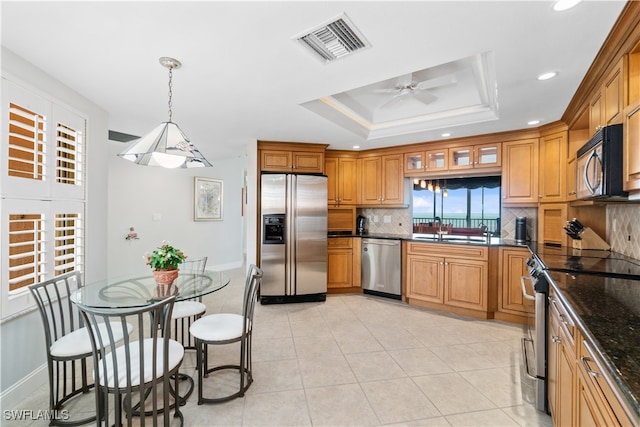 kitchen featuring dark stone countertops, pendant lighting, stainless steel appliances, ceiling fan, and sink