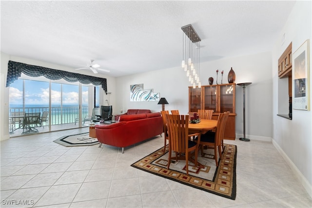 dining space featuring a textured ceiling, a water view, light tile patterned flooring, and ceiling fan