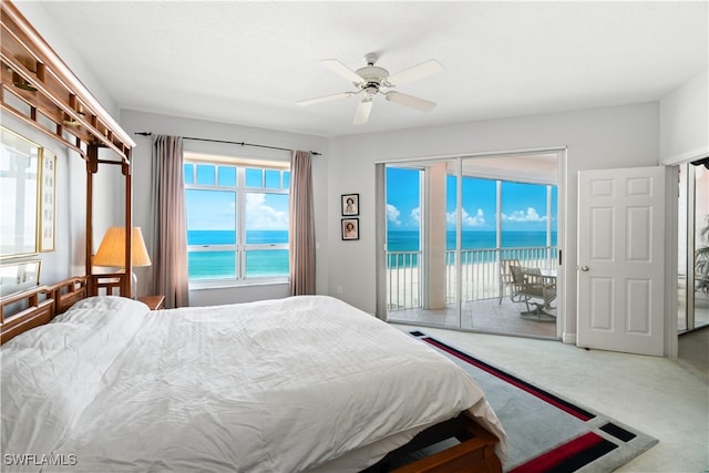 carpeted bedroom featuring a water view, a beach view, ceiling fan, and access to exterior